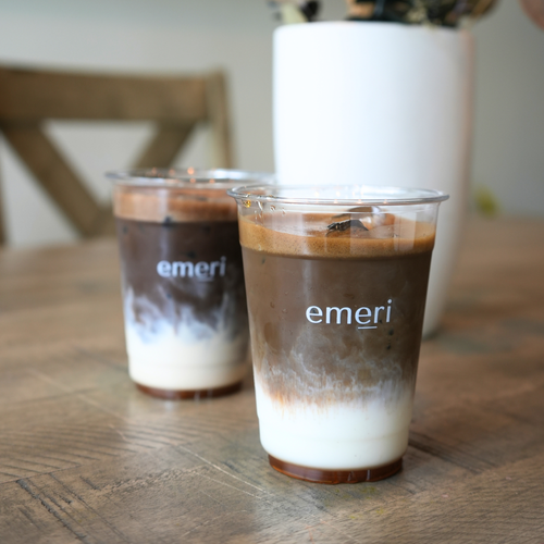 Two glasses of emeri hojicha on a wooden table with a blurred background